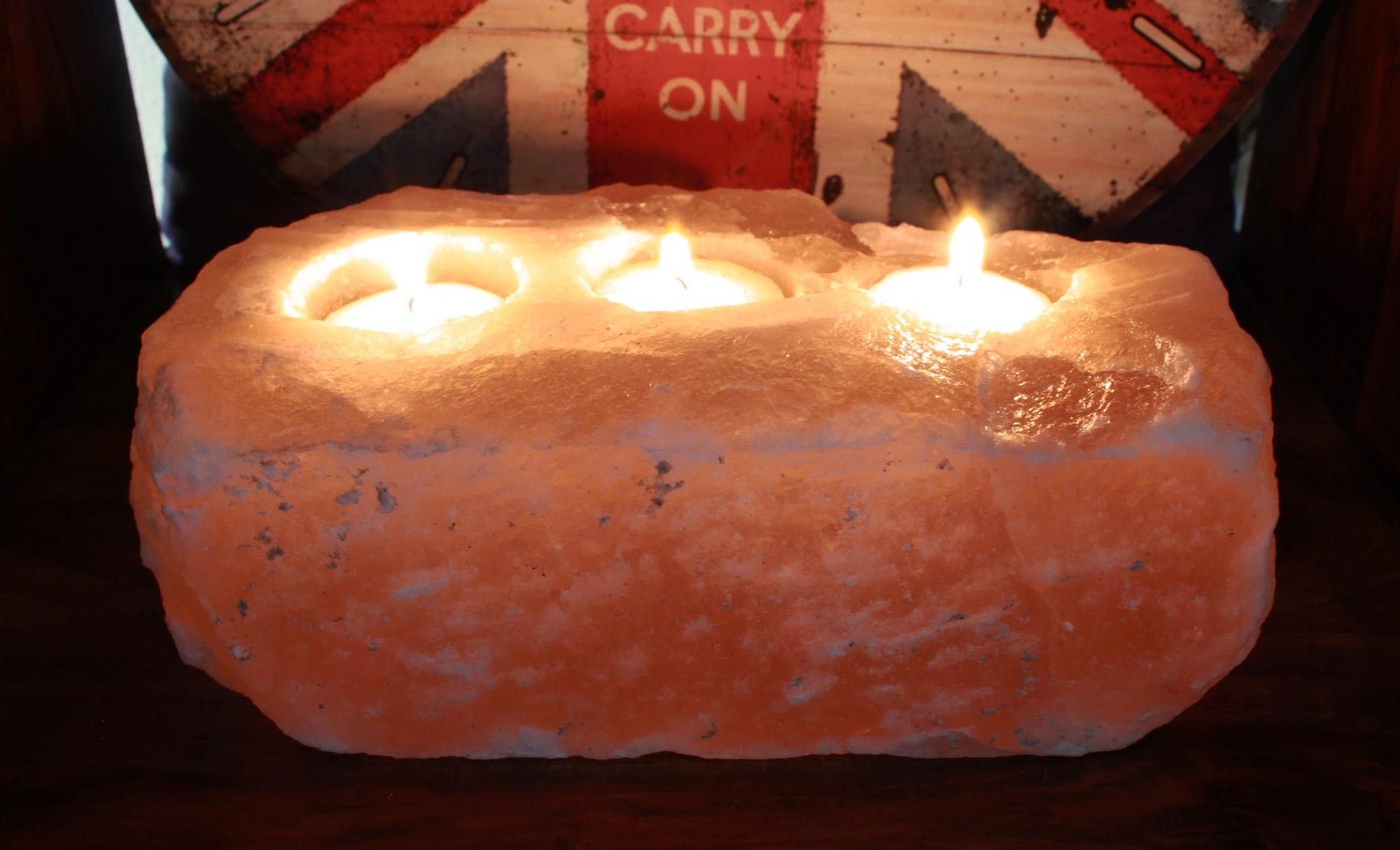 A rectangular block of raw, natural pink Himalayan salt featuring three carved holes for tealight candles.
