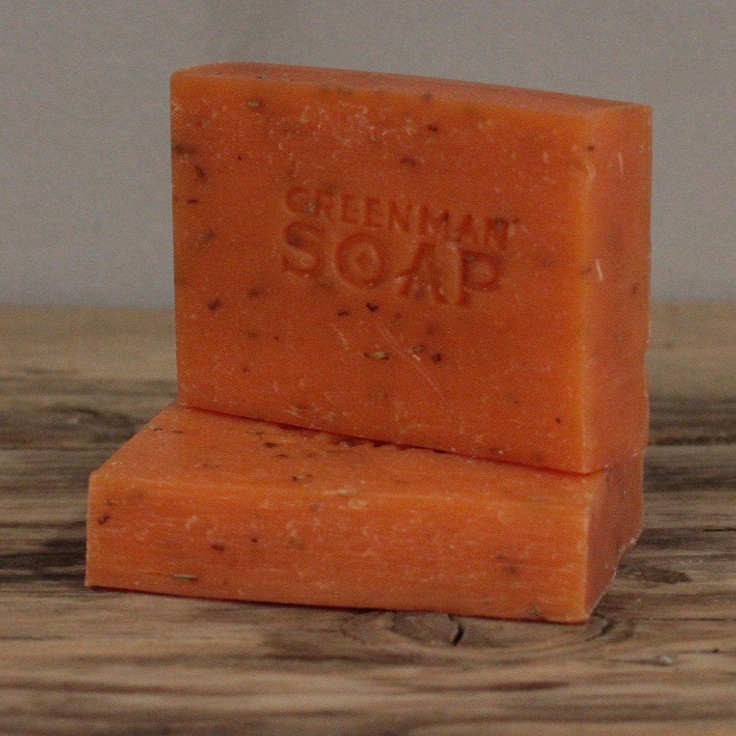 handcrafted orange Greenman artisan soap slices flecked with real dried rosemary leaves, presented on a natural wood surface.