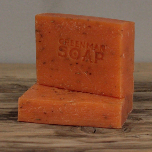 handcrafted orange Greenman artisan soap slices flecked with real dried rosemary leaves, presented on a natural wood surface.