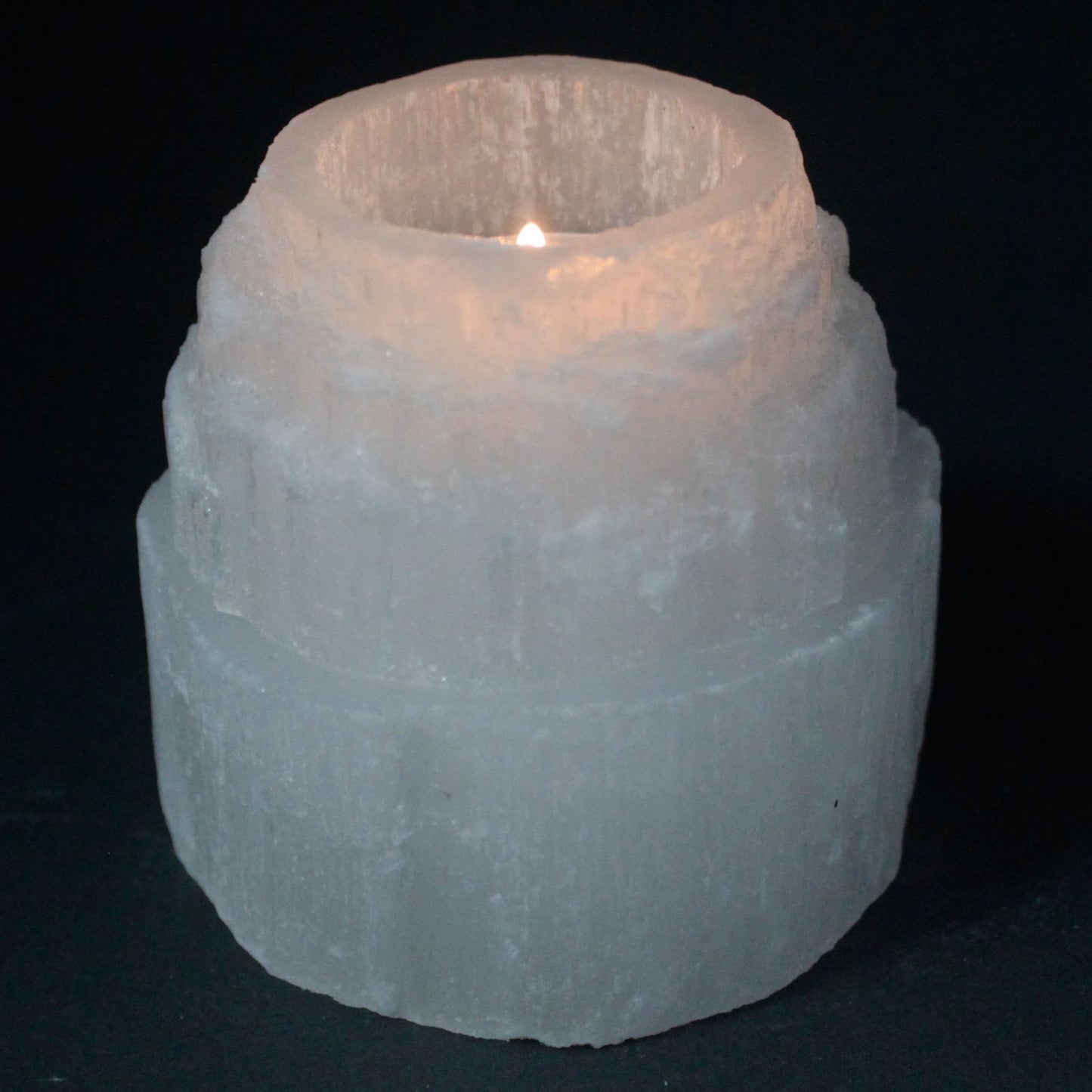 A natural, cloudy-white Selenite crystal carved into a tiered mountain top shape, featuring a polished top with a hollow centre designed to hold a tealight.