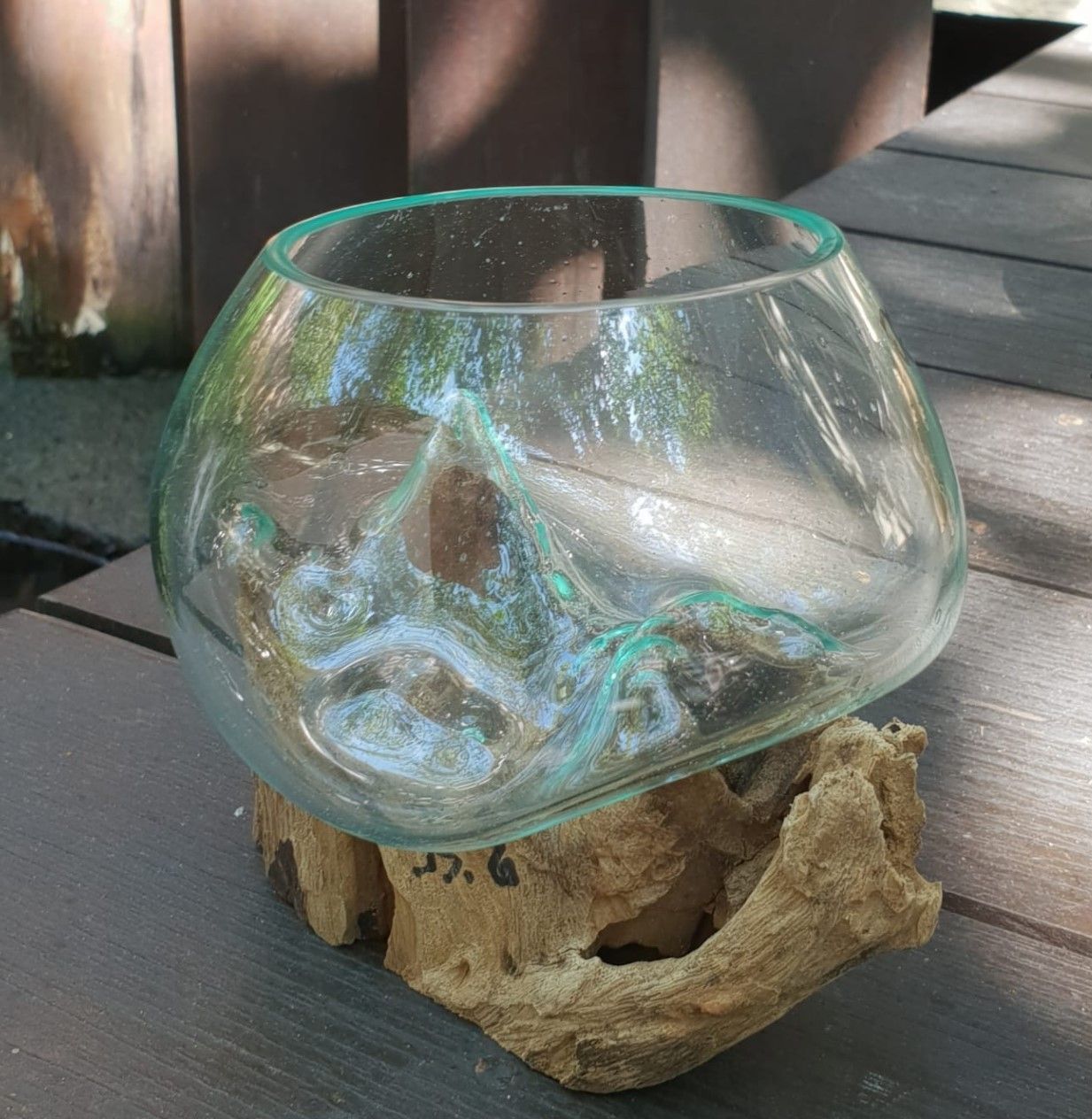 A small, rounded hand-blown glass bowl resting perfectly on the natural, uneven contours of a piece of reclaimed root wood.