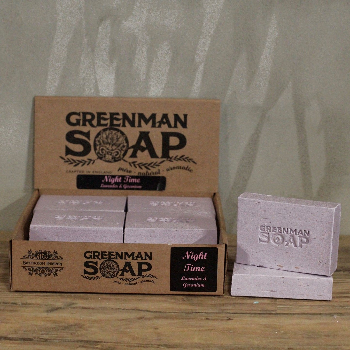 Handcrafted light purple Greenman artisan soap slices featuring dried lavender flowers, presented on a natural wood surface.