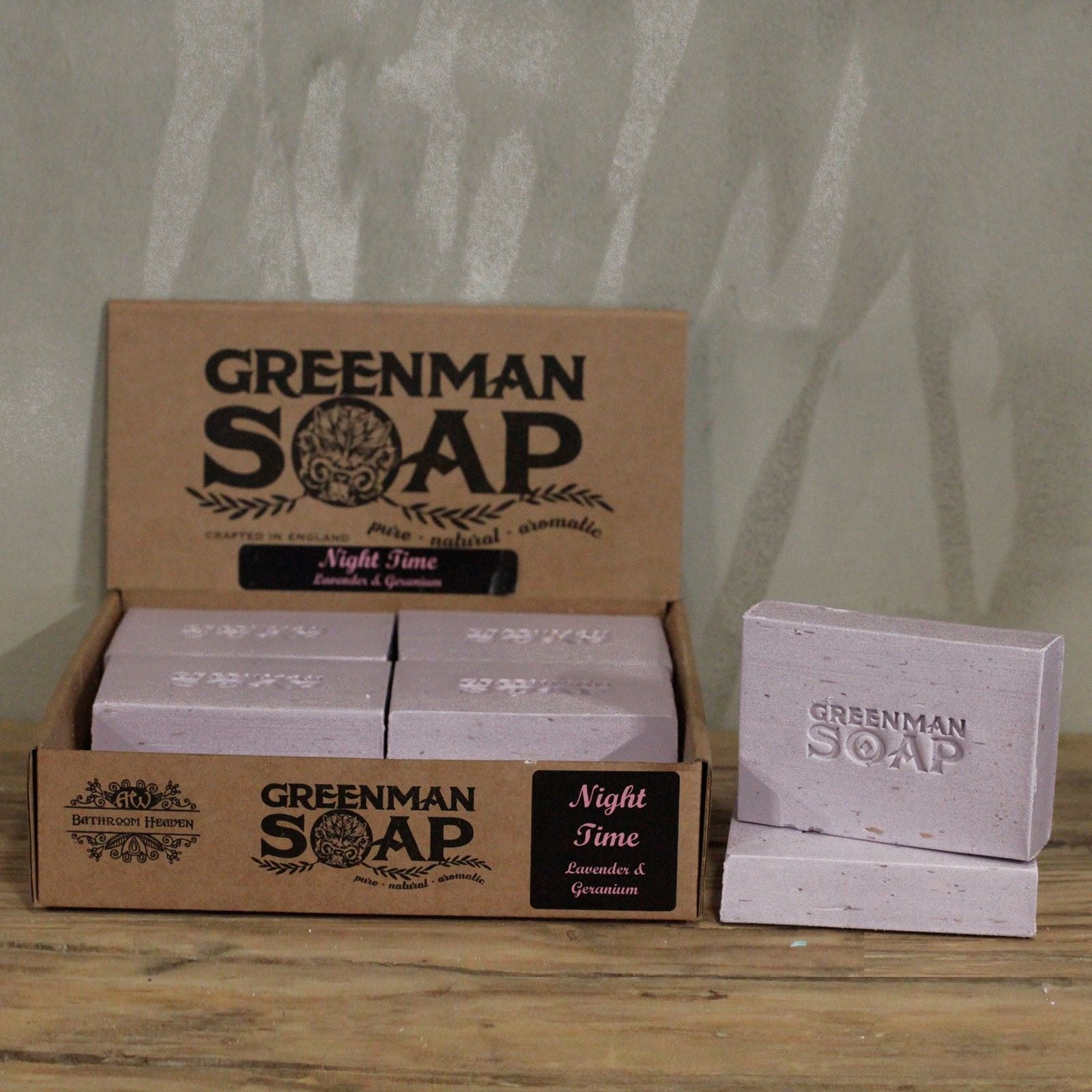 Handcrafted light purple Greenman artisan soap slices featuring dried lavender flowers, presented on a natural wood surface.