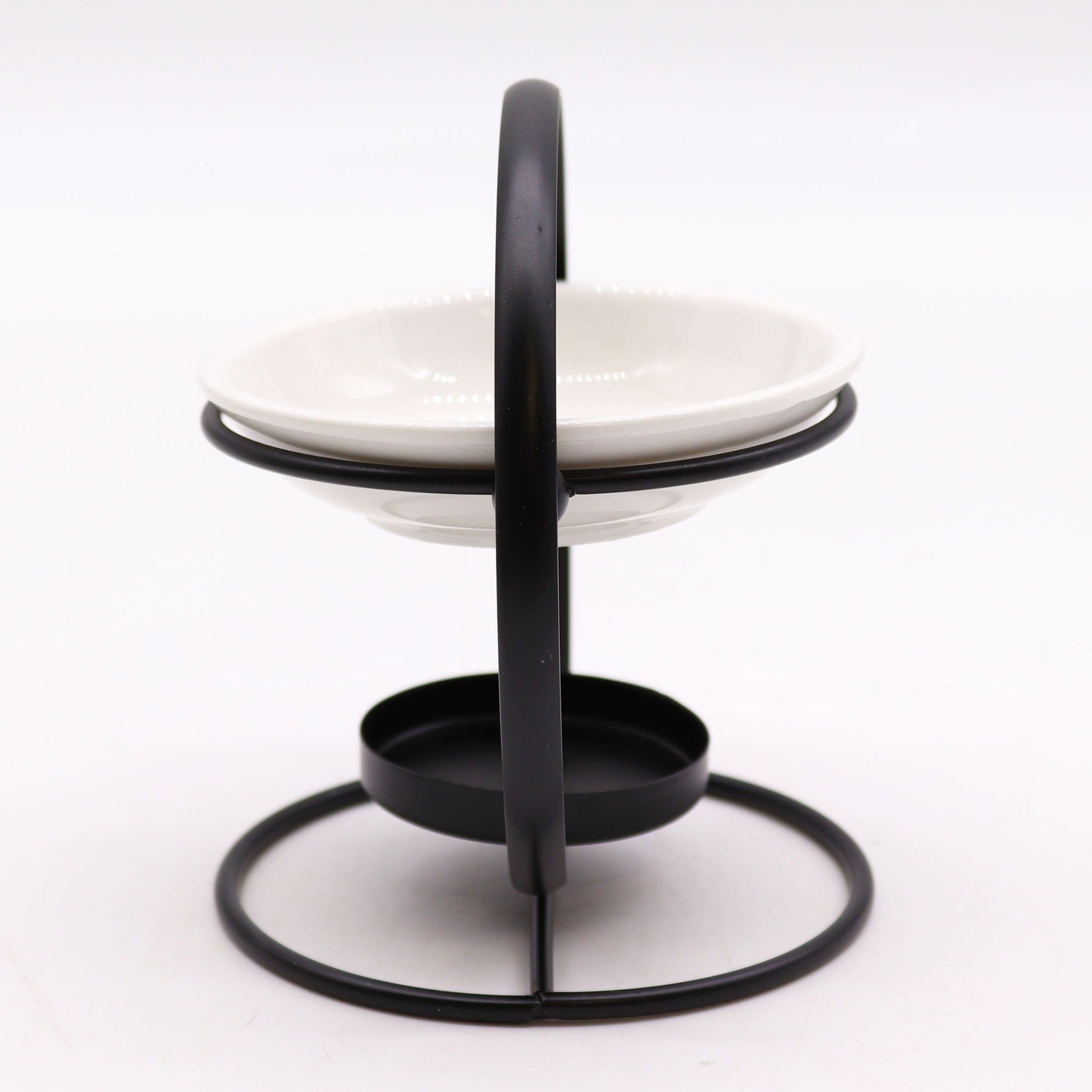 A modern essential oil burner featuring a circular black metal frame holding a shallow white ceramic bowl, with a small tealight holder at the base.