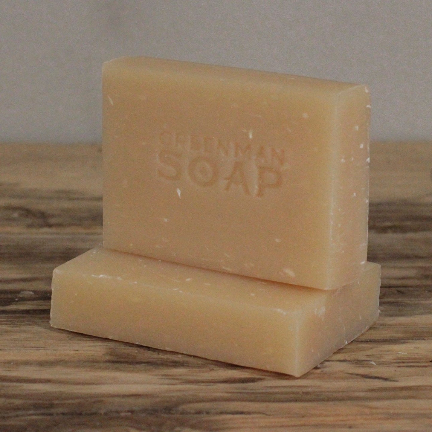 handcrafted creamy white Greenman artisan soap slices featuring dried coconut flakes, presented on a natural wood surface.
