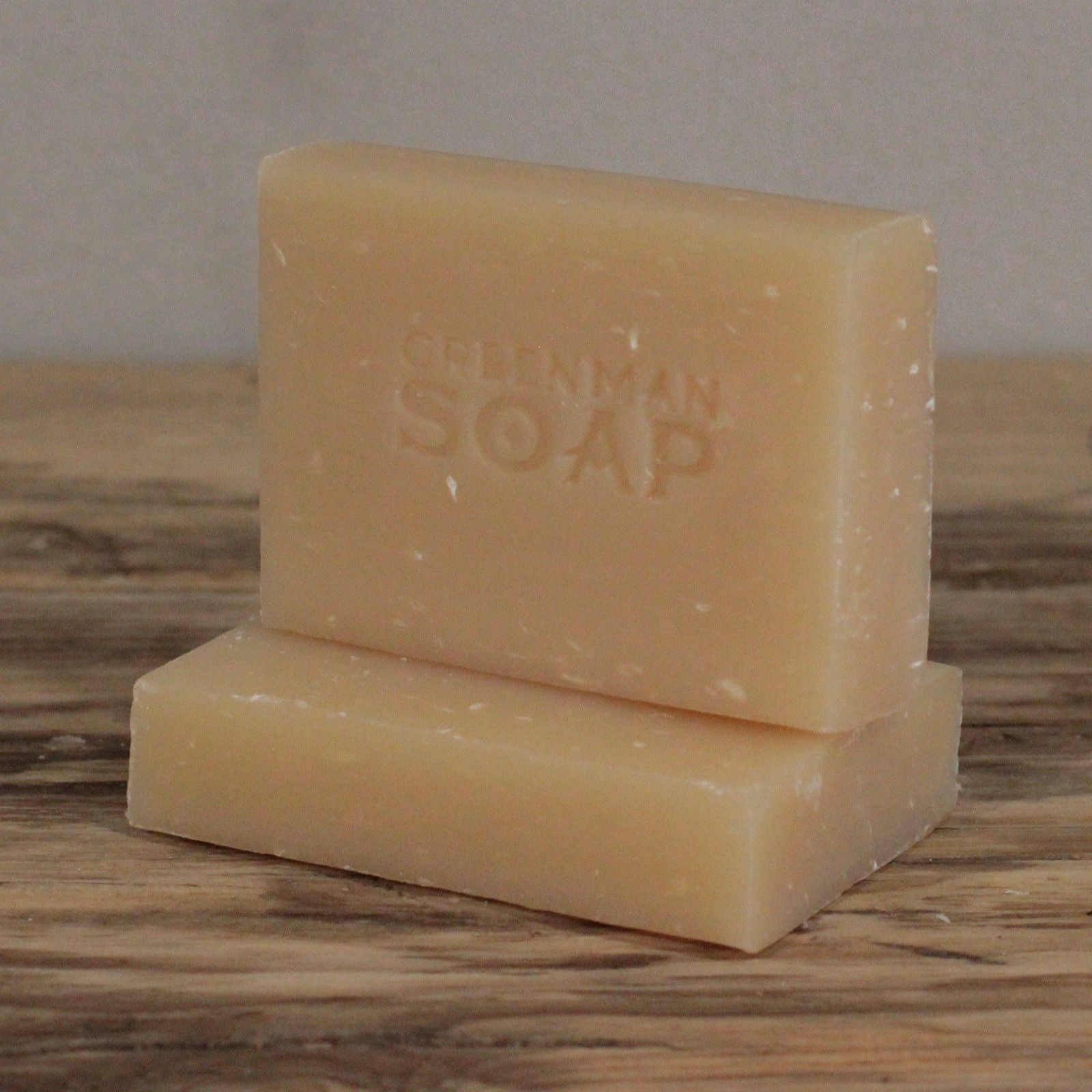 handcrafted creamy white Greenman artisan soap slices featuring dried coconut flakes, presented on a natural wood surface.