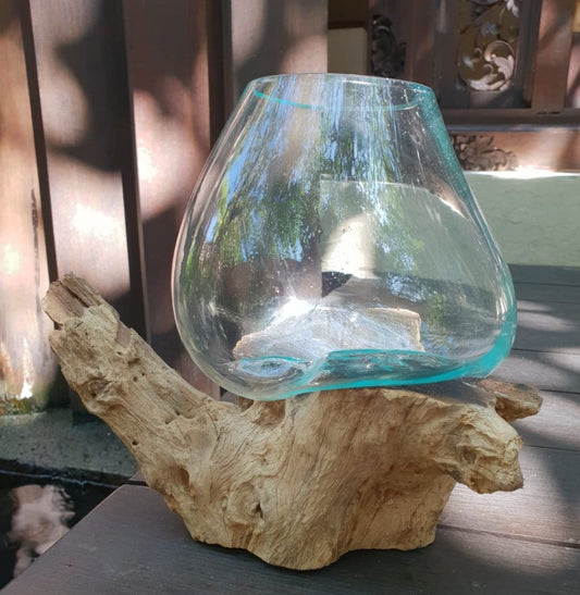 A large hand-blown glass bowl resting perfectly on the natural, uneven contours of a chunky piece of raw reclaimed root wood.