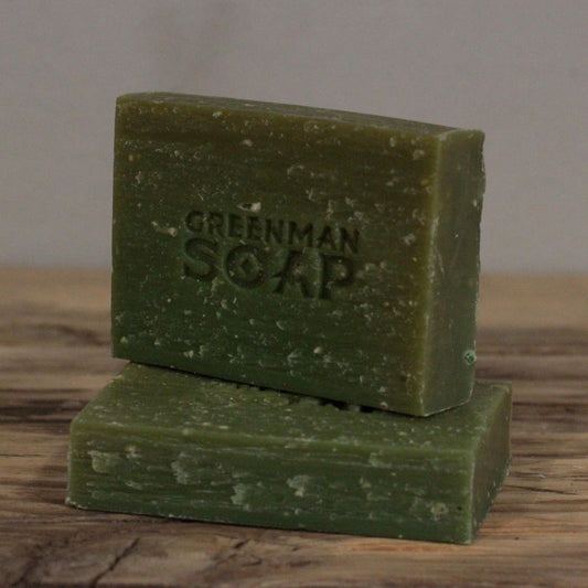 Handcrafted olive-green Greenman artisan soap slices featuring natural pumice texture, presented on a natural wood surface.